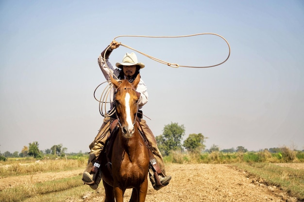 Retrato de um cowboy segurando uma corda enquanto monta um cavalo em terra
