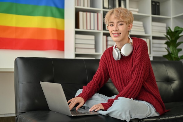 Retrato de um criativo freelancer gay asiático está trabalhando em casa usando seu laptop em um sofá