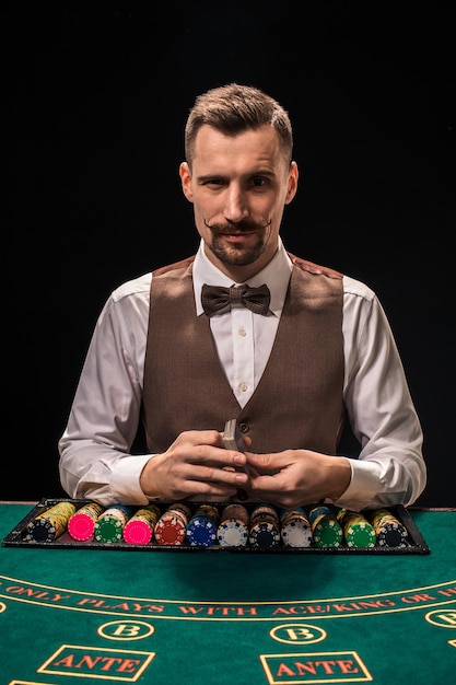Retrato de um crupiê segurando fichas de jogo de cartas de jogar no fundo preto da mesa