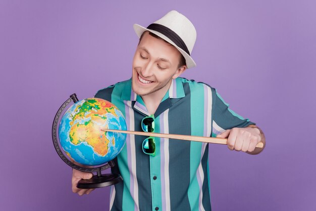 Retrato de um curioso turista charmoso segurando um globo indica um ponteiro que olha a África em fundo violeta