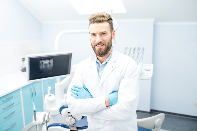 Retrato de um dentista bonito de uniforme no consultório odontológico