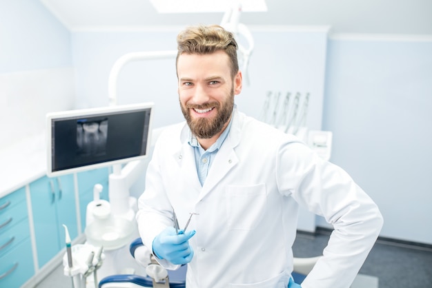 Retrato de um dentista bonito de uniforme no consultório odontológico
