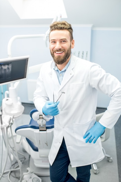 Retrato de um dentista bonito de uniforme no consultório odontológico