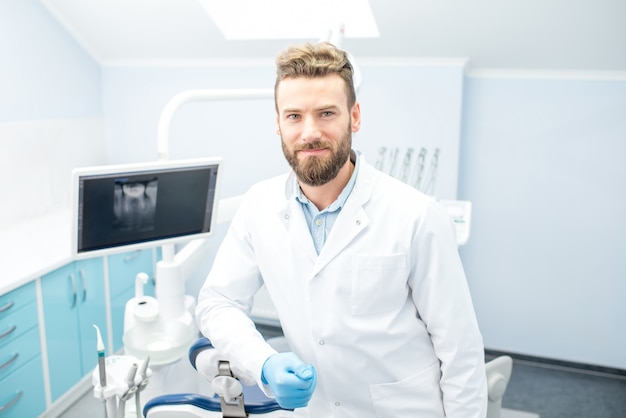Retrato de um dentista bonito de uniforme no consultório odontológico