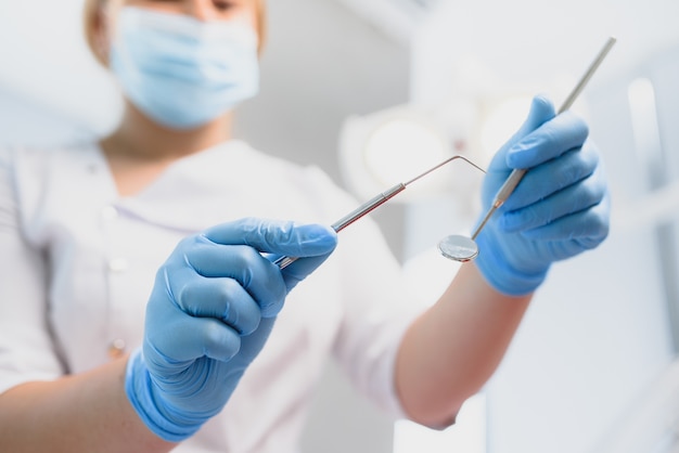 Retrato de um dentista segurando instrumentos odontológicos nas mãos em close-up da clínica