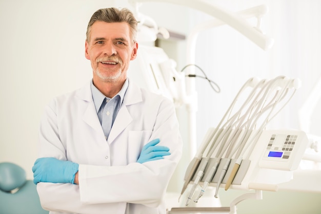 Retrato de um dentista sênior sorridente na clínica odontológica.