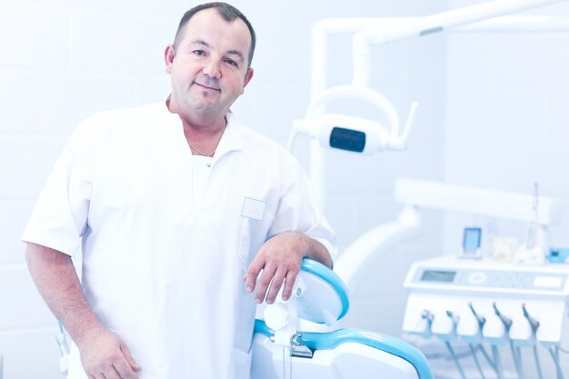 Foto retrato de um dentista sorridente em pé na clínica odontológica