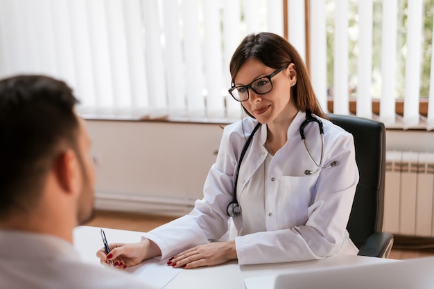 Retrato de um doutor fêmea bonito que escreve uma prescrição médica a um paciente com um sorriso.