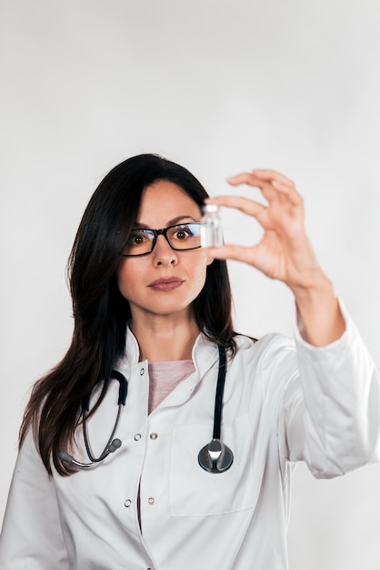 Retrato de um doutor fêmea bonito que guarda o frasco da medicina para a injeção.