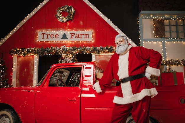 Retrato de um elegante Papai Noel perto do carro com presentes. Preparando presentes para a celebração do Natal e Ano Novo