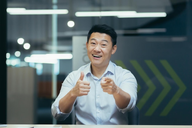 Retrato de um empresário asiático bem-sucedido e feliz, ele se senta no escritório na mesa de trabalho