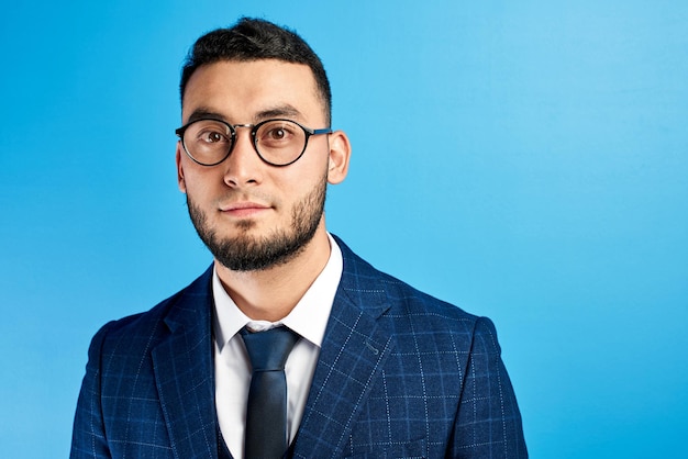 Retrato de um empresário asiático de sucesso bonito do Cazaquistão sorridente de terno e óculos no fundo azul do estúdio isolado