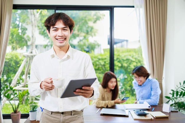 Retrato de um empresário asiático inteligente segurando um tablet digital em casa com sua equipe de negócios