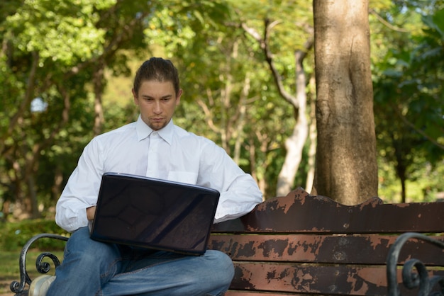 Retrato de um empresário barbudo bonito com cabelo comprido relaxando no parque ao ar livre