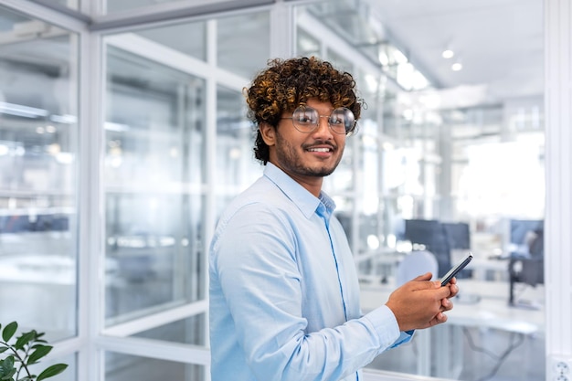 Retrato de um empresário bem-sucedido dentro de um escritório moderno e brilhante indiano sorrindo e olhando para