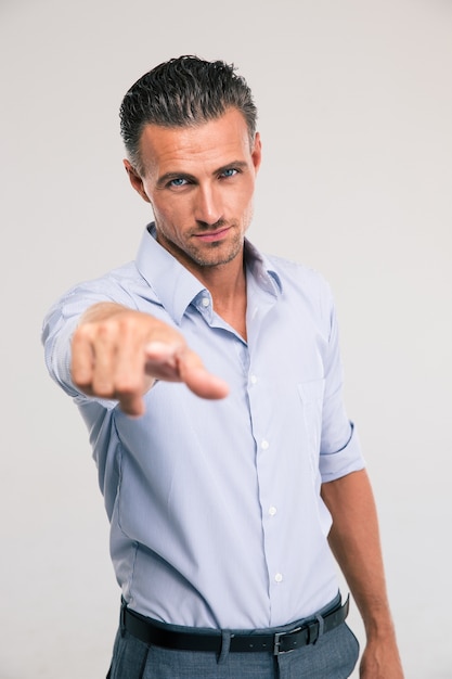 Retrato de um empresário bonitão apontando o dedo para a câmera no espaço cinza