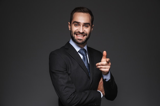 Retrato de um empresário bonito e confiante vestindo terno isolado, apontando o dedo para a frente