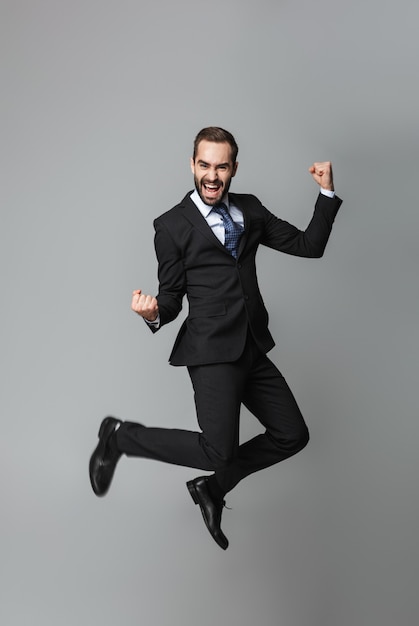 Retrato de um empresário bonito e confiante vestindo terno isolado, pulando, comemorando o sucesso
