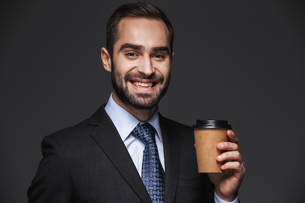 Retrato de um empresário bonito e confiante vestindo terno isolado, segurando uma xícara para viagem