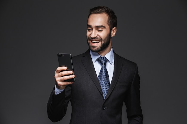 Retrato de um empresário bonito e confiante vestindo um terno de pé isolado, usando telefone celular