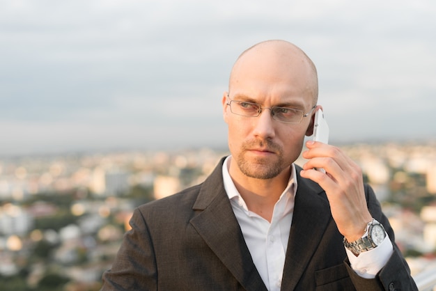 Retrato de um empresário careca bonito com a barba por fazer contra a vista da cidade ao ar livre