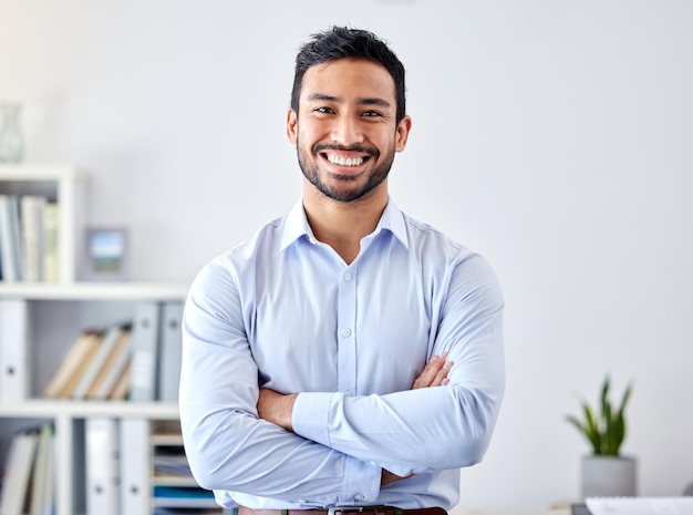 Retrato de um empresário com um sorriso em um escritório corporativo moderno de uma empresa startup carreira feliz e gerente profissional ou empresário em pé com os braços cruzados em seu espaço de trabalho