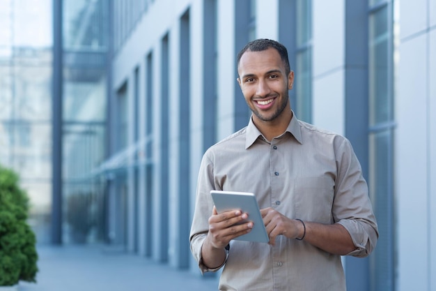 Retrato de um empresário feliz do lado de fora de um prédio de escritórios, um homem de camisa casual está olhando para o