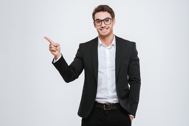 Retrato de um empresário feliz em óculos apontando o dedo sobre uma parede branca