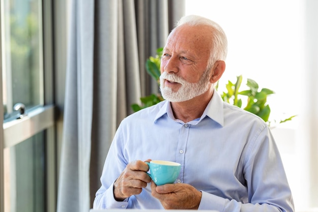 Retrato de um empresário sênior sorridente segurando uma caneca de café olhando através da janela fechar o espaço livre