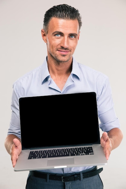 Retrato de um empresário sorridente mostrando a tela do laptop em branco isolada