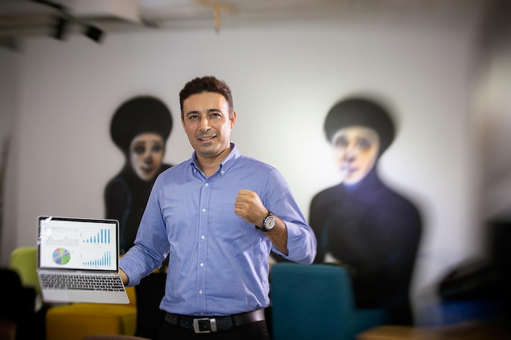 Foto retrato de um empresário sorridente segurando um laptop enquanto está de pé no escritório