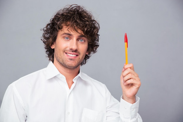 Retrato de um empresário sorridente segurando uma caneta sobre uma parede cinza