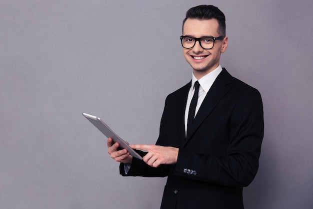 Retrato de um empresário sorridente usando um computador tablet sobre uma parede cinza