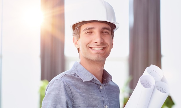 Retrato de um engenheiro com um capacete e plantas em suas mãos posando