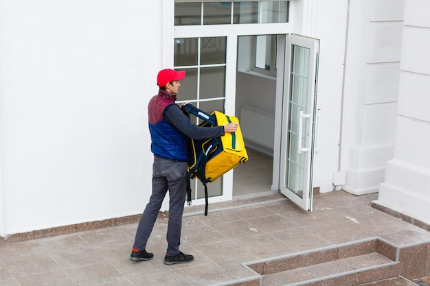 Retrato de um entregador alegre em pé com uma mochila térmica amarela para entrega de comida na rua ao ar livre