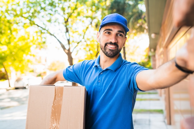 Retrato de um entregador carregando pacotes enquanto toca a campainha para fazer entrega em domicílio ao seu cliente. Entrega e conceito de envio.