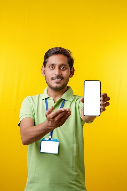 Foto retrato de um entregador jovem feliz animado em t-shirt e apresentando smartphone sobre fundo amarelo.