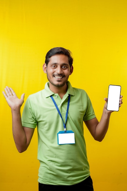 Retrato de um entregador jovem feliz animado em t-shirt e apresentando smartphone sobre fundo amarelo.