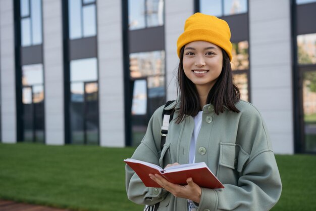 Retrato de um estudante asiático de sucesso sorridente segurando o livro olhando para a câmera no campus universitário