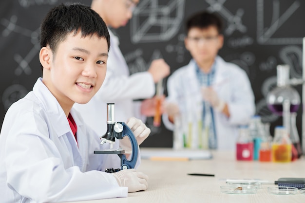 Retrato de um estudante asiático sorridente com microscópio na aula de química