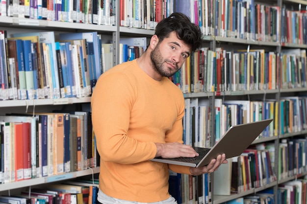 Retrato de um estudante atraente fazendo algum trabalho escolar com um laptop na biblioteca