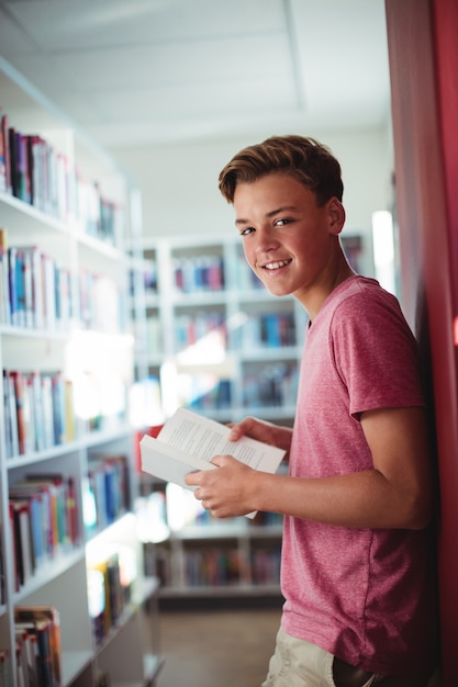 Retrato de um estudante feliz segurando um livro na biblioteca