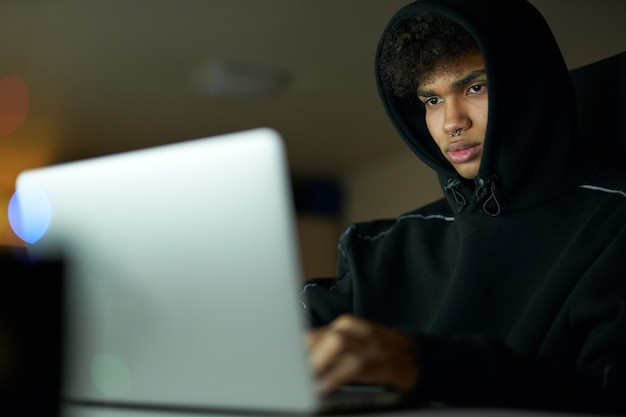 Retrato de um estudante ocupado estudando, trabalhando em um laptop, sentado em casa tarde da noite