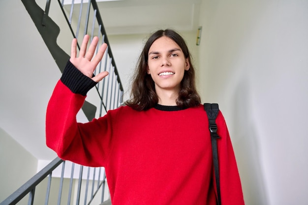 Retrato de um estudante sorridente com mochila acenando com a mão