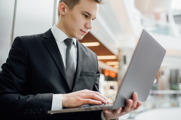 Retrato de um estudante trabalhando em um laptop, vestido de terno preto em um shopping