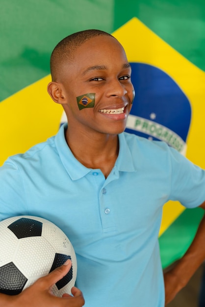 Foto retrato de um feliz adolescente afro-americano com bandeira do brasil e futebol