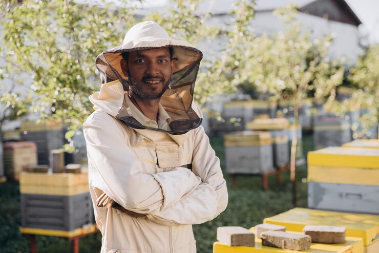 Retrato de um feliz apicultor indiano trabalhando em um apiário perto de colmeias com abelhas Coletar mel