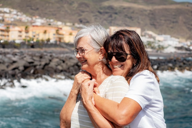 Retrato de um feliz casal caucasiano sênior de mulheres se abraçando em férias no mar abraçando