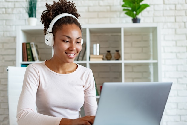 Retrato, de, um, feliz, mulatto, mulher, freelancer, trabalhar, laptop, em, fones ouvido, e, escutar música