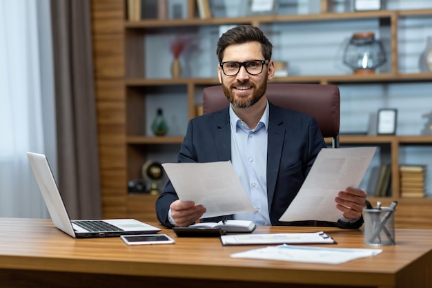 Retrato de um financista bem-sucedido com documentos nas mãos, sorrindo e olhando para a câmera